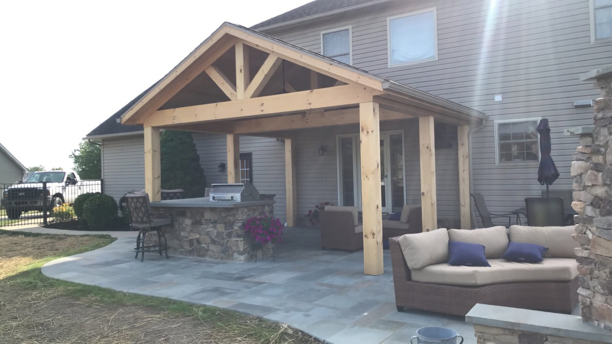 A timber-frame covered patio with a stone bar and outdoor furniture